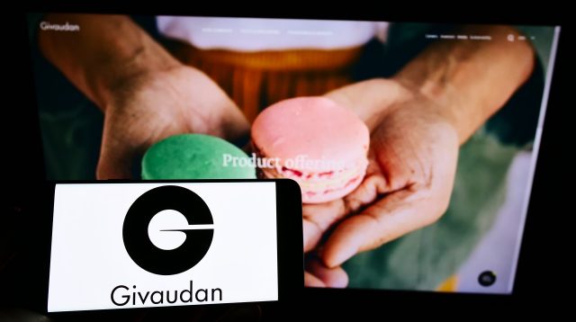 Eine Person hält ein Mobiltelefon mit dem Logo des Aromen- und Duftstoffherstellers Givaudan S.A. auf dem Bildschirm vor einer Webseite mit Fokus auf das Telefondisplay