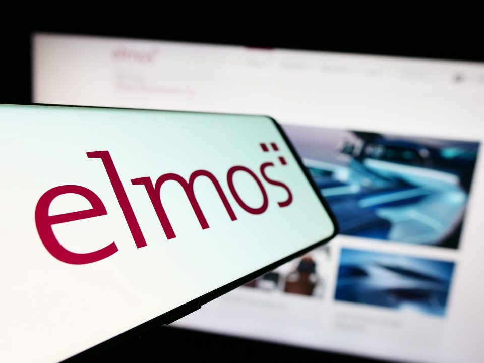 Mobiltelefon mit dem Logo der deutschen Firma Elmos Semiconductor SE auf dem Bildschirm vor einer Unternehmenswebsite mit Fokus auf die Mitte links des Telefondisplays