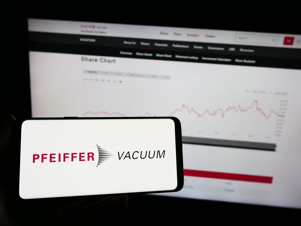 Eine Person hält ein Mobiltelefon mit dem Logo der deutschen Firma Pfeiffer Vacuum Technology AG auf dem Bildschirm vor einer Webseite mit Fokus auf das Telefondisplay
