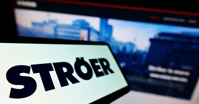 Mobiltelefon mit Logo der deutschen Werbefirma Ströer SE Co. KGaA auf dem Bildschirm vor einer Unternehmenswebsite mit Fokus auf der linken Seite des Telefondisplays