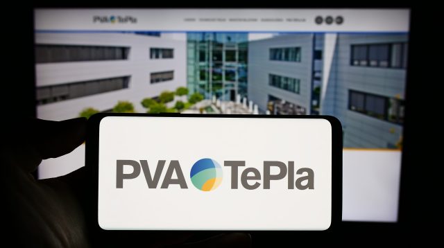 Eine Person hält ein Mobiltelefon mit dem Logo des deutschen Technologieunternehmens PVA TePla AG auf dem Bildschirm vor einer Geschäftswebseite mit Fokus auf das Telefondisplay