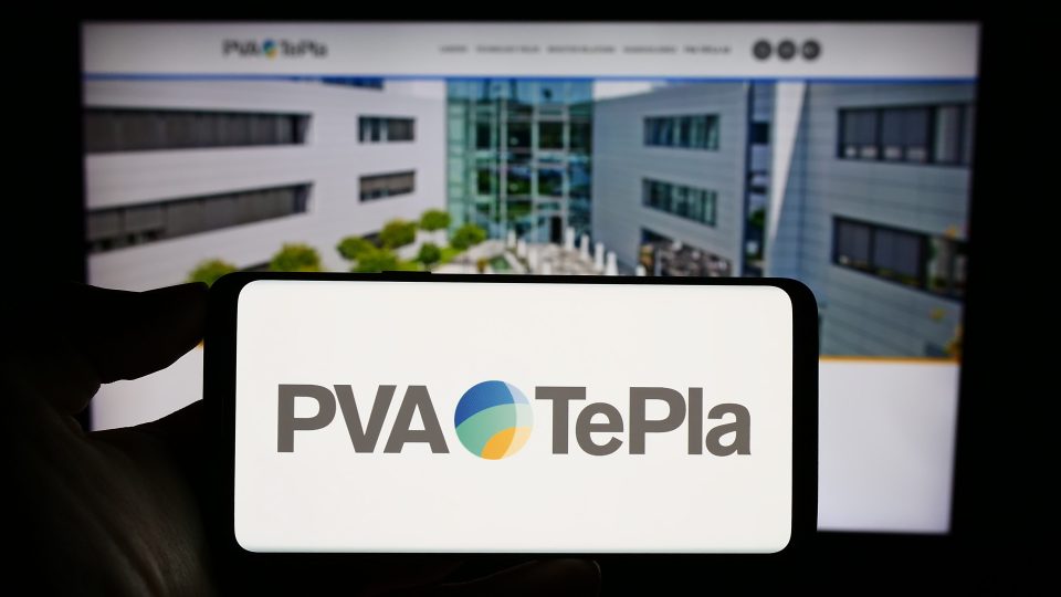 Eine Person hält ein Mobiltelefon mit dem Logo des deutschen Technologieunternehmens PVA TePla AG auf dem Bildschirm vor einer Geschäftswebseite mit Fokus auf das Telefondisplay