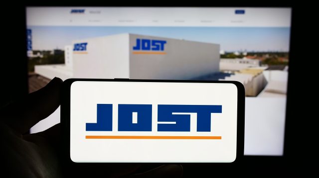 Eine Person hält ein Smartphone mit dem Logo von Jost Werke auf dem Bildschirm vor einer Website mit Fokus auf das Telefondisplay