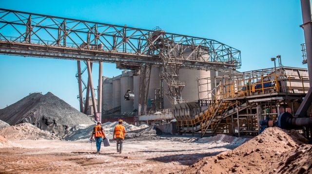 Moderne Zementproduktion: Industriemitarbeiter zwischen Anlagen, Sand- und Rohstoffhaufen