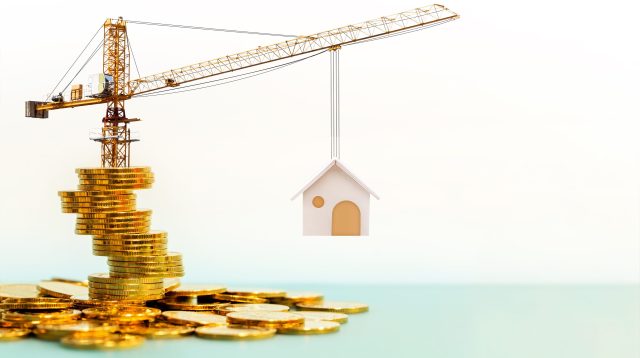 Kran steht auf Goldmünzen und hebt Haus hoch