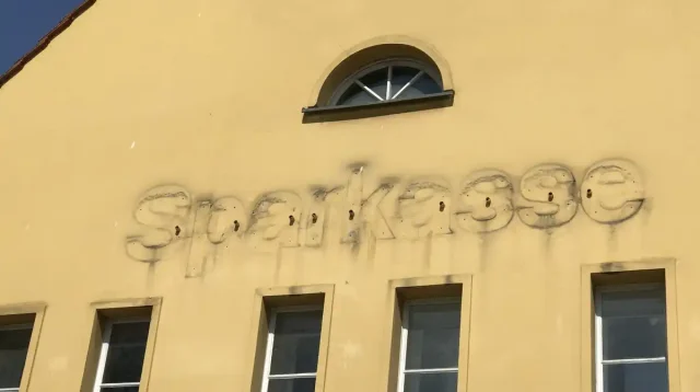An einer gelben Hauswand wurde der Schriftzug "Sparkasse" entfernt. Die Abdrücke der alten Buchstaben sind noch deutlich zu sehen.