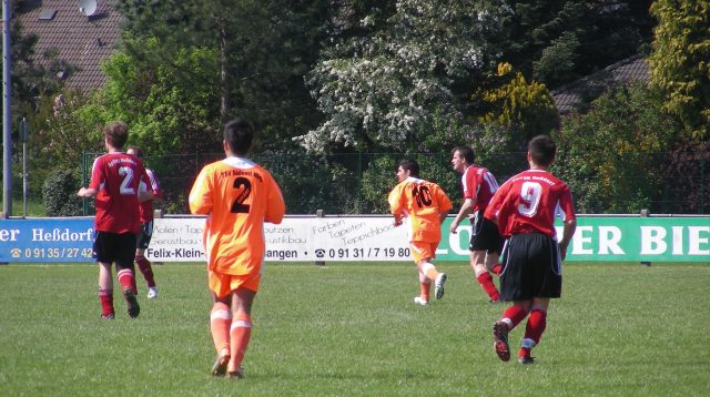 Fußballturnier eines lokalen Vereins: Jungen in roten und orangen Trikots spielen auf einem Fußballplatz Fußball.